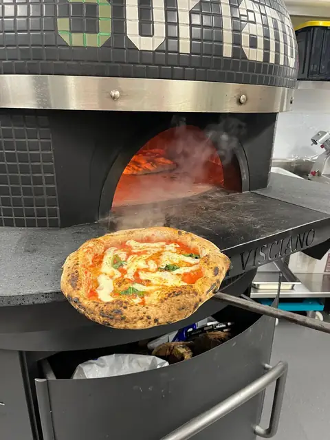 A pizza on the peel, coming out of the wood-fire oven