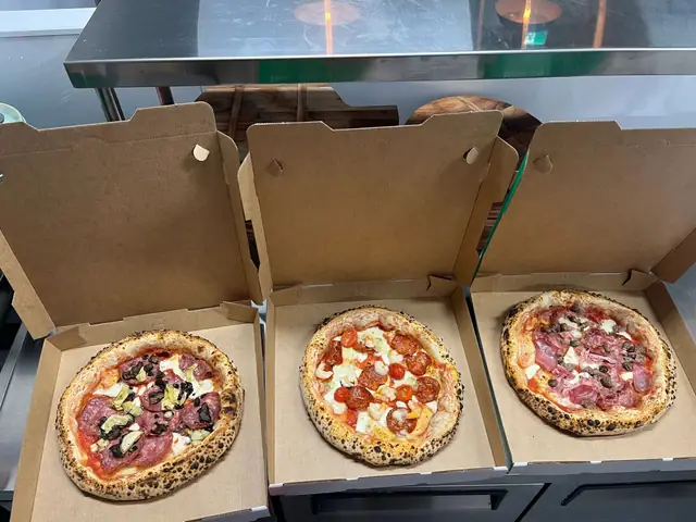 Three pizzas in takeaway boxes
